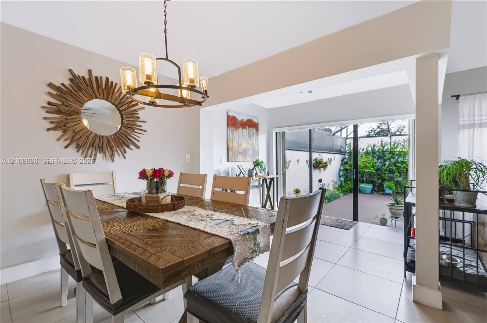 9123 SW 117th Court, Miami, FL 33186 Dining area featuring large-format tile flooring, a circular multi-light chandelier, and sliding glass doors providing outdoor access to a private paved courtyard