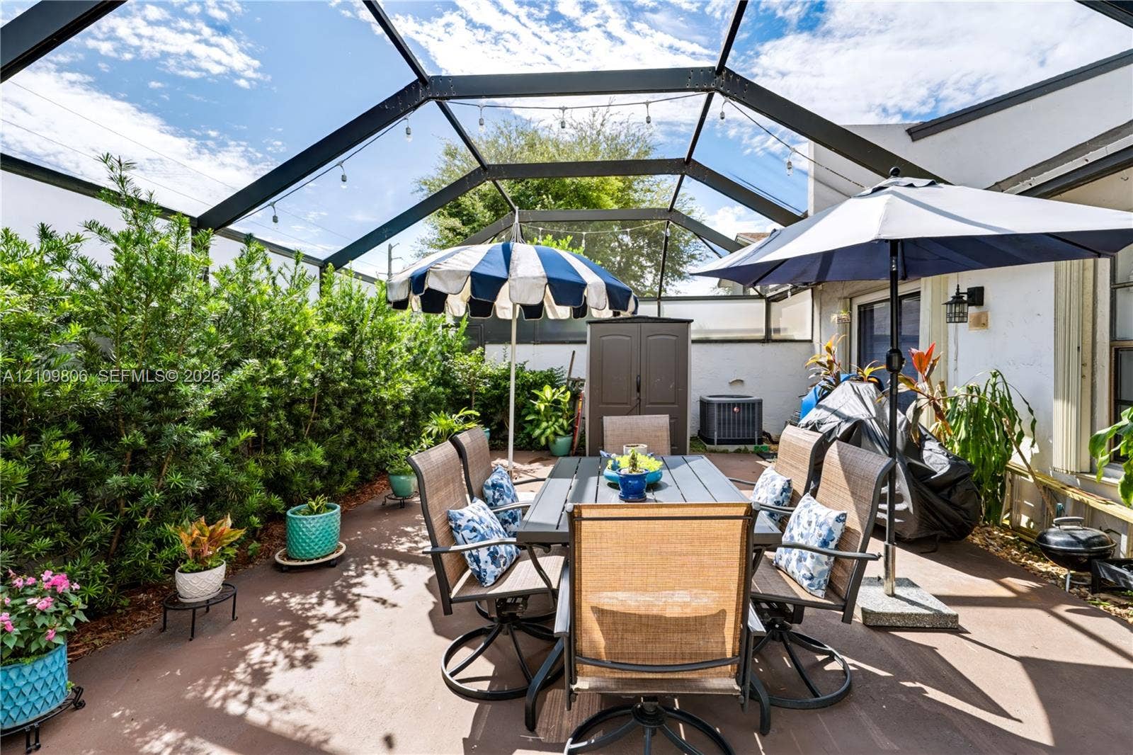 9123 SW 117th Court, Miami, FL 33186 Screened-in patio featuring a concrete floor, privacy hedge, and wall-mounted exterior lighting