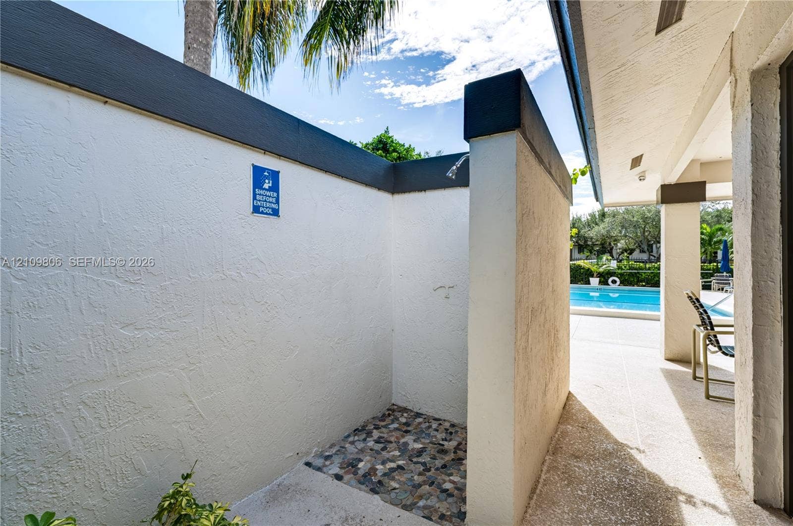 9123 SW 117th Court, Miami, FL 33186 Outdoor shower area featuring textured privacy walls, a pebble-stone floor, and a wall-mounted showerhead