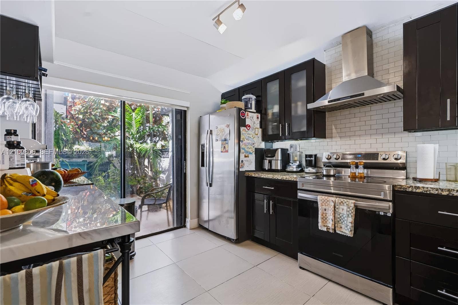 9123 SW 117th Court, Miami, FL 33186 Kitchen featuring espresso cabinetry, stone countertops, stainless steel appliances, white subway tile backsplash, and sliding glass doors