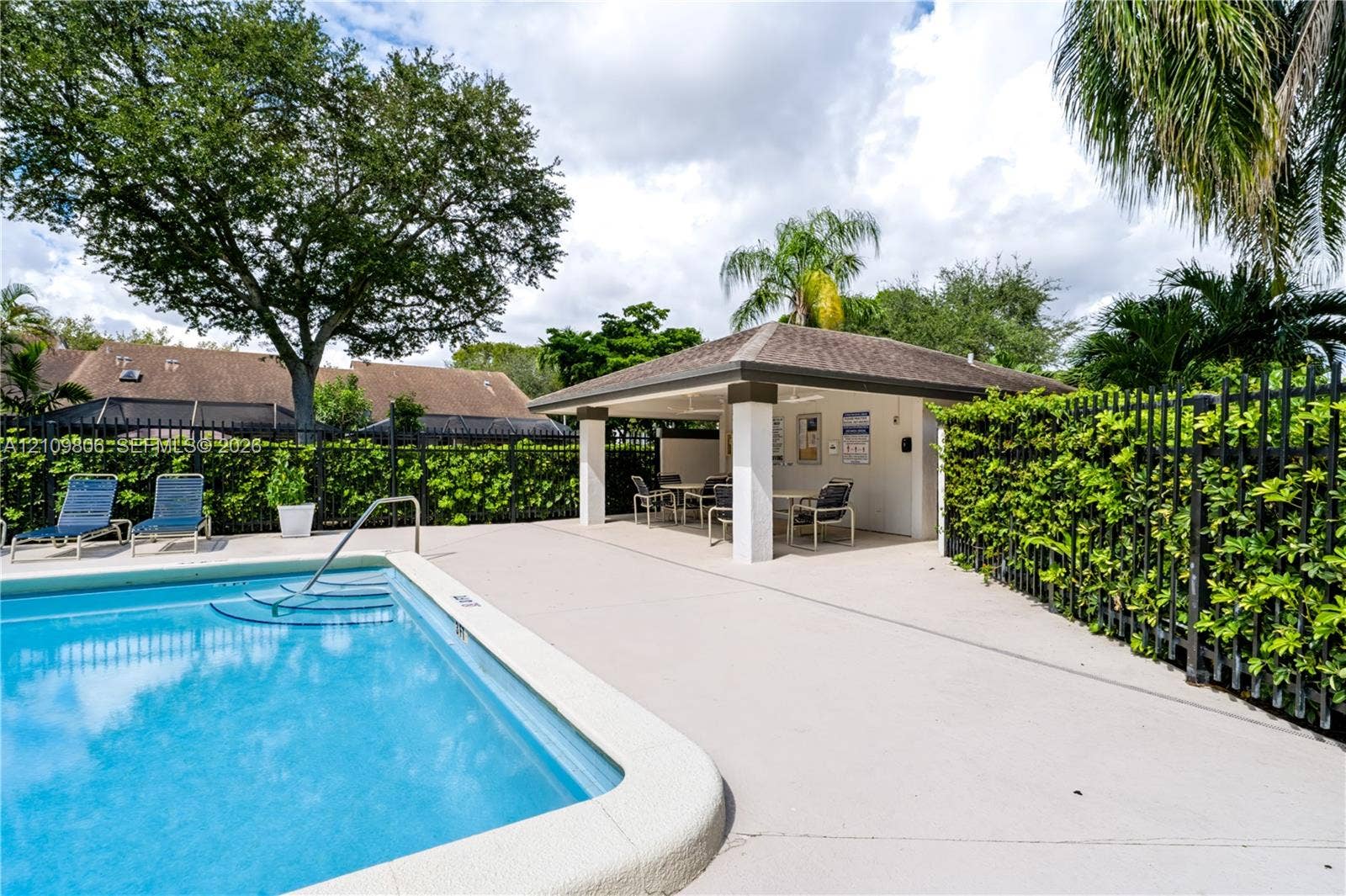 9123 SW 117th Court, Miami, FL 33186 Swimming pool with an integrated metal handrail, expansive concrete deck, and a covered pavilion featuring structural pillars