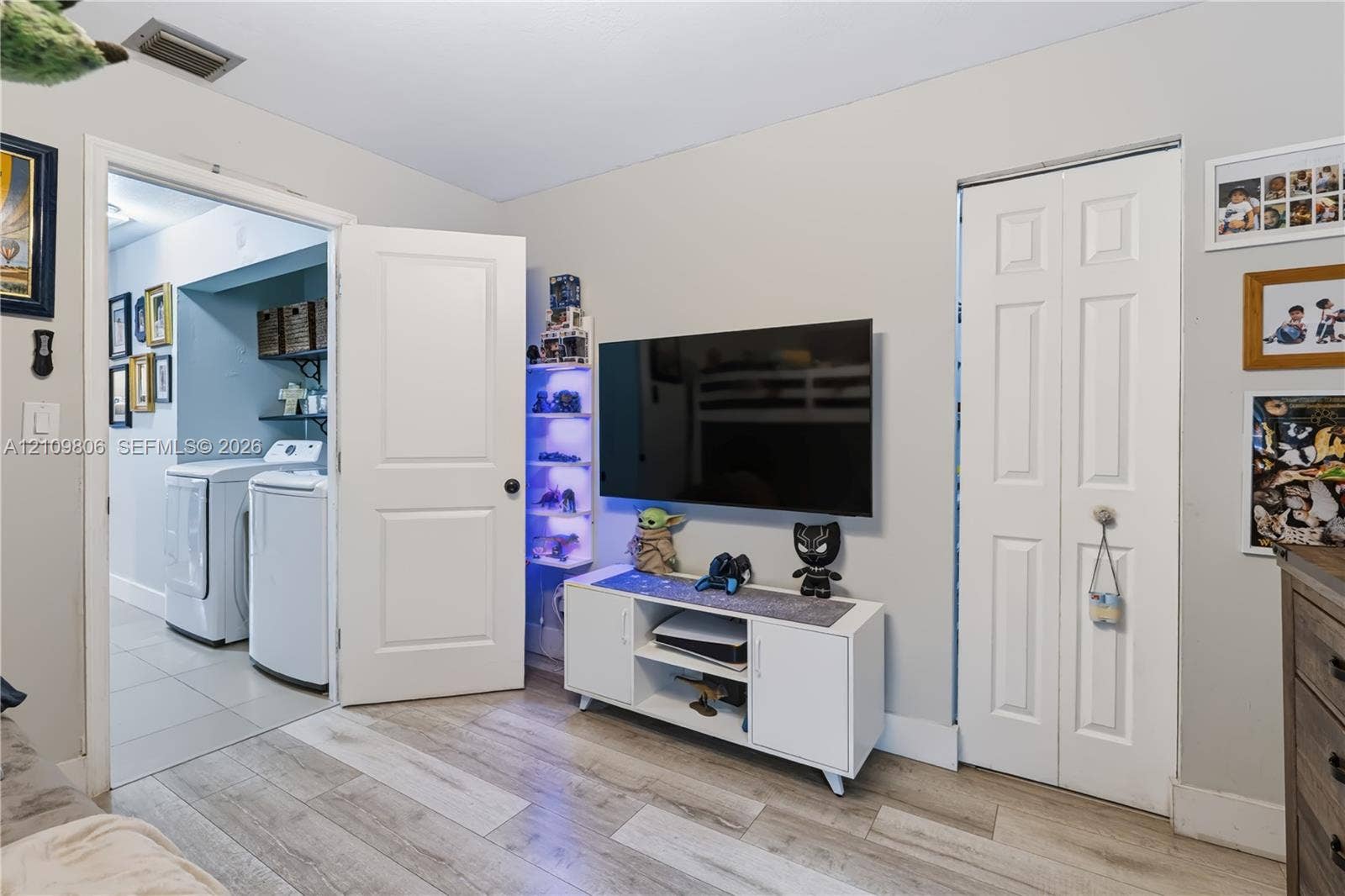 9123 SW 117th Court, Miami, FL 33186 Interior room featuring wood-finish flooring, a bi-fold closet, and a standard interior door opening to a laundry area with tile flooring and built-in shelving