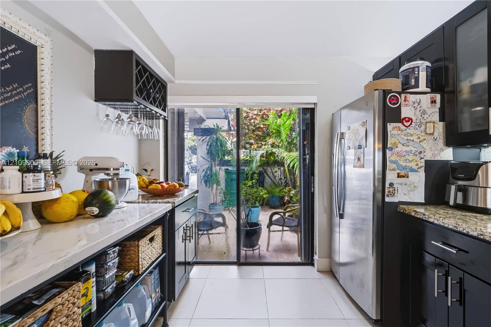 9123 SW 117th Court, Miami, FL 33186 Kitchen featuring dark cabinetry, stone-finish countertops, stainless steel refrigerator, built-in stemware rack, and glass sliding doors
