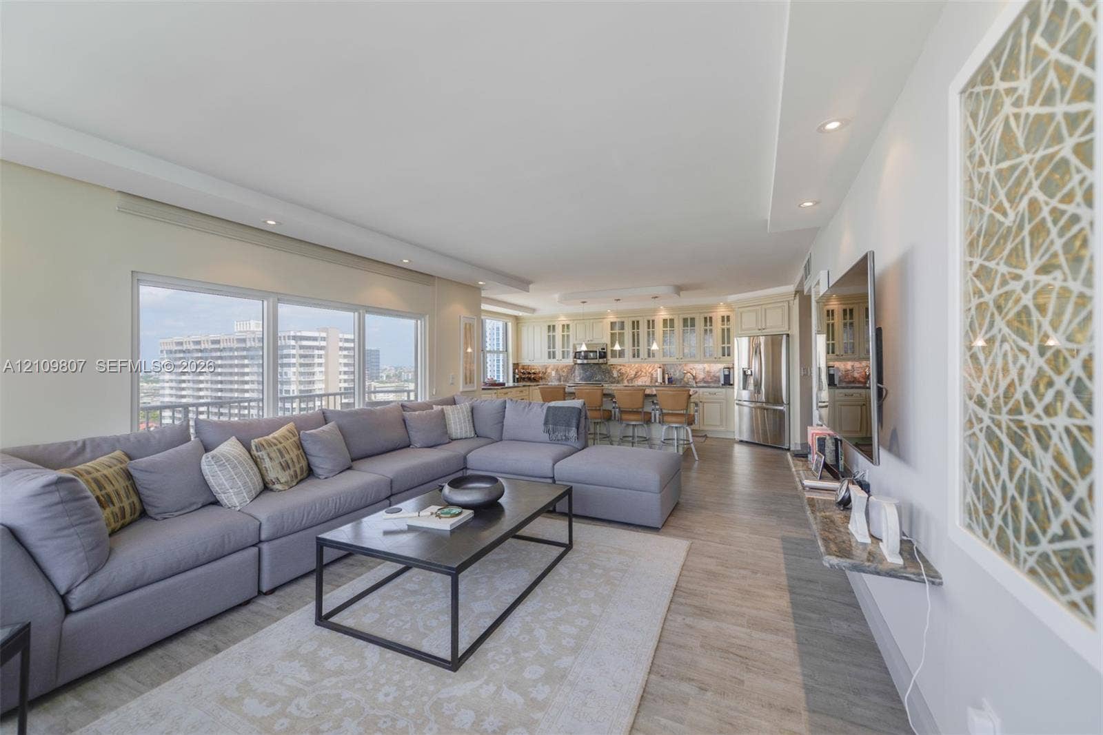 1980 S Ocean Drive, #16Q, Hallandale Beach, FL 33009 Open-concept main living area featuring wood-finish flooring, recessed lighting, floor-to-ceiling windows, built-in kitchen cabinetry, and a stone-topped wall-mounted shelf
