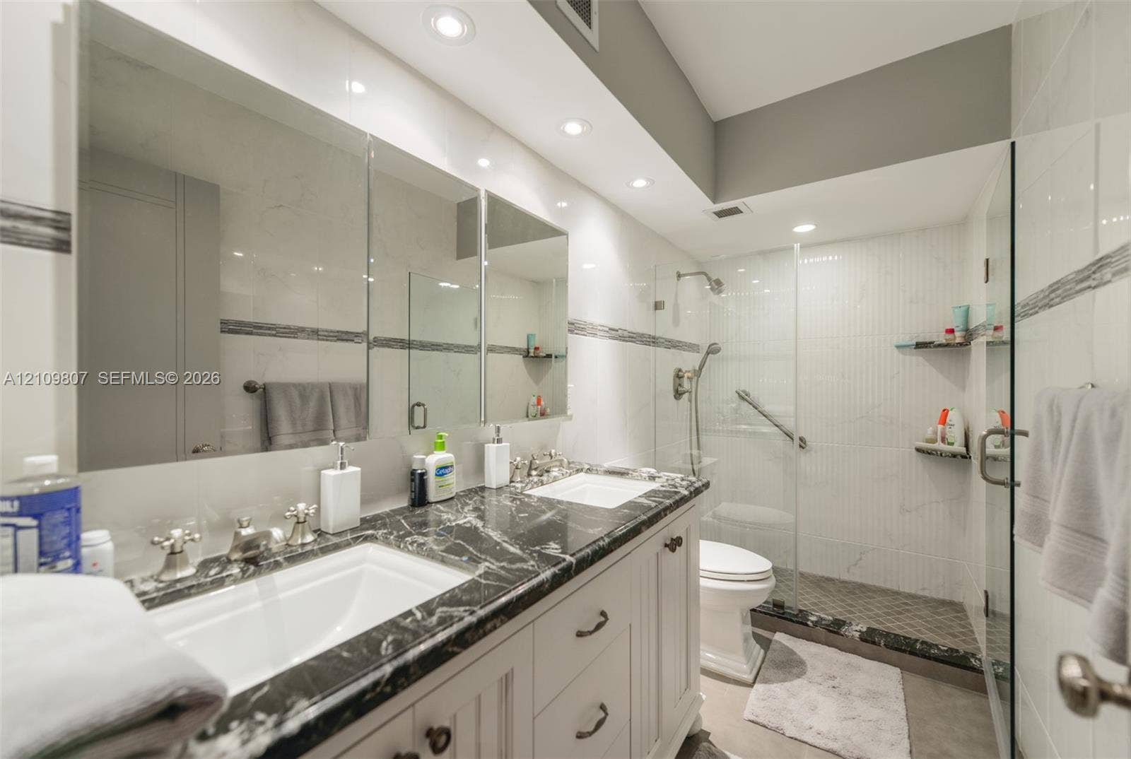 1980 S Ocean Drive, #16Q, Hallandale Beach, FL 33009 Dual-sink vanity with stone countertop, recessed lighting, expansive wall-to-wall mirror, and glass-enclosed shower with tiled surround
