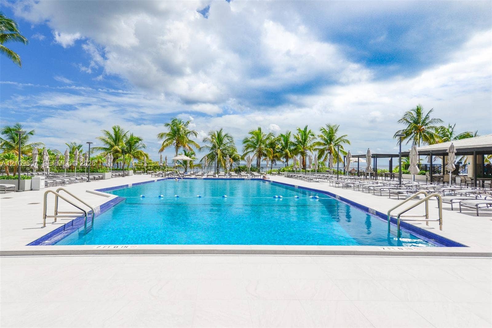 1980 S Ocean Drive, #16Q, Hallandale Beach, FL 33009 Large swimming pool with tiled perimeter, metal handrails, and a wide paved deck surrounded by mature palm trees