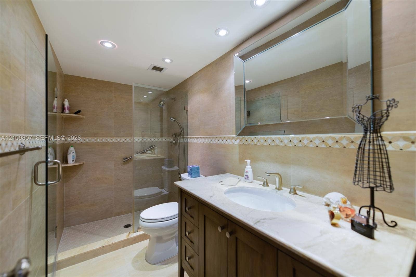 1980 S Ocean Drive, #16Q, Hallandale Beach, FL 33009 Bathroom featuring a vanity with stone countertop, beveled-edge wall mirror, recessed ceiling lighting, and a glass-enclosed shower with tiled walls
