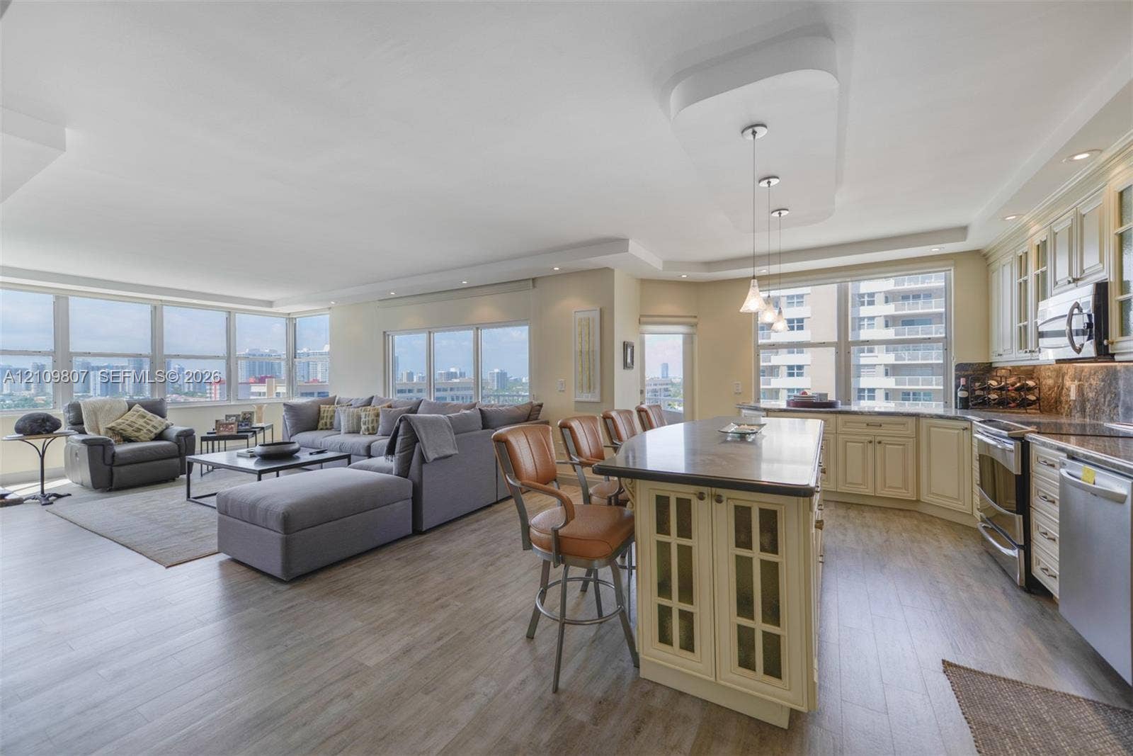 1980 S Ocean Drive, #16Q, Hallandale Beach, FL 33009 Open-concept kitchen featuring an expansive island with stone-surface countertop, custom cabinetry with glass-paneled detailing, stainless steel appliances, and wood-finish flooring throughout