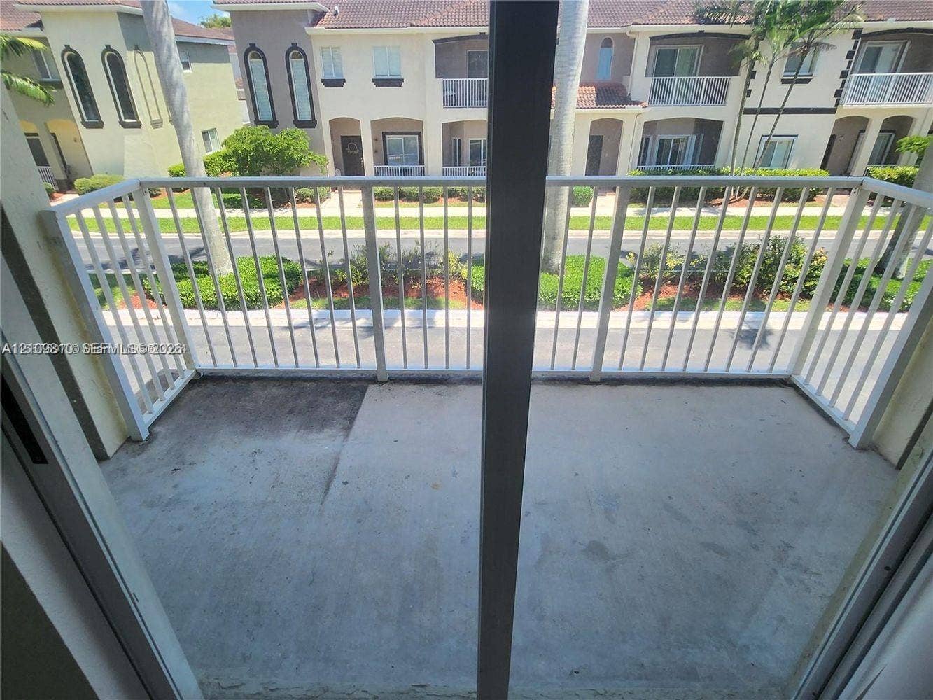 Concrete balcony with a white metal railing and sliding glass door entrance
