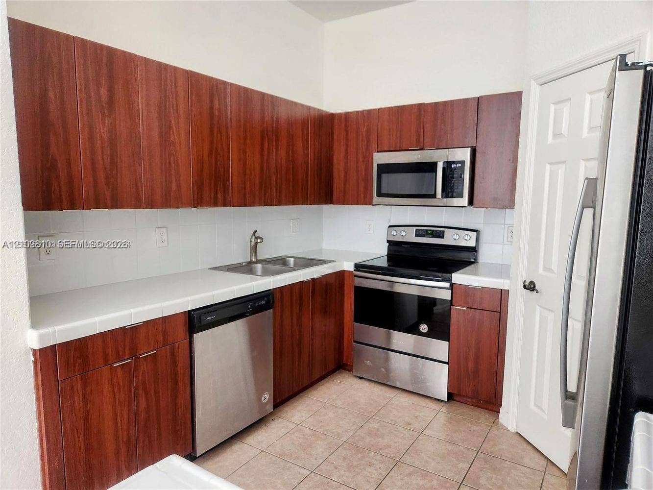 Kitchen featuring wood-finish cabinetry, white tile countertops, stainless steel appliances, and ceramic tile flooring