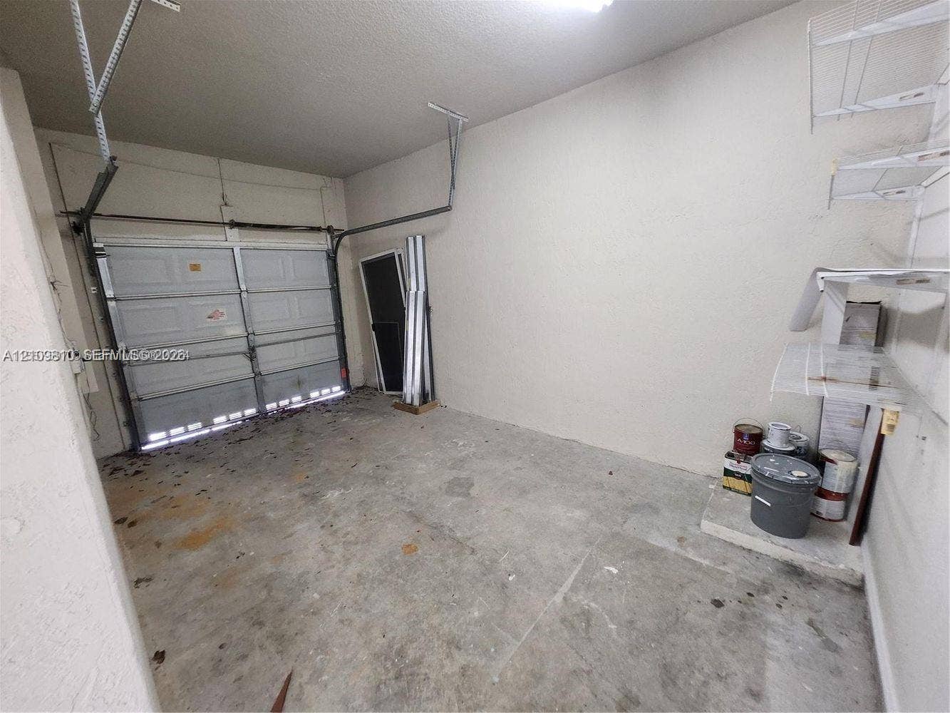 Enclosed garage featuring concrete flooring, a sectional overhead door, and wall-mounted wire shelving