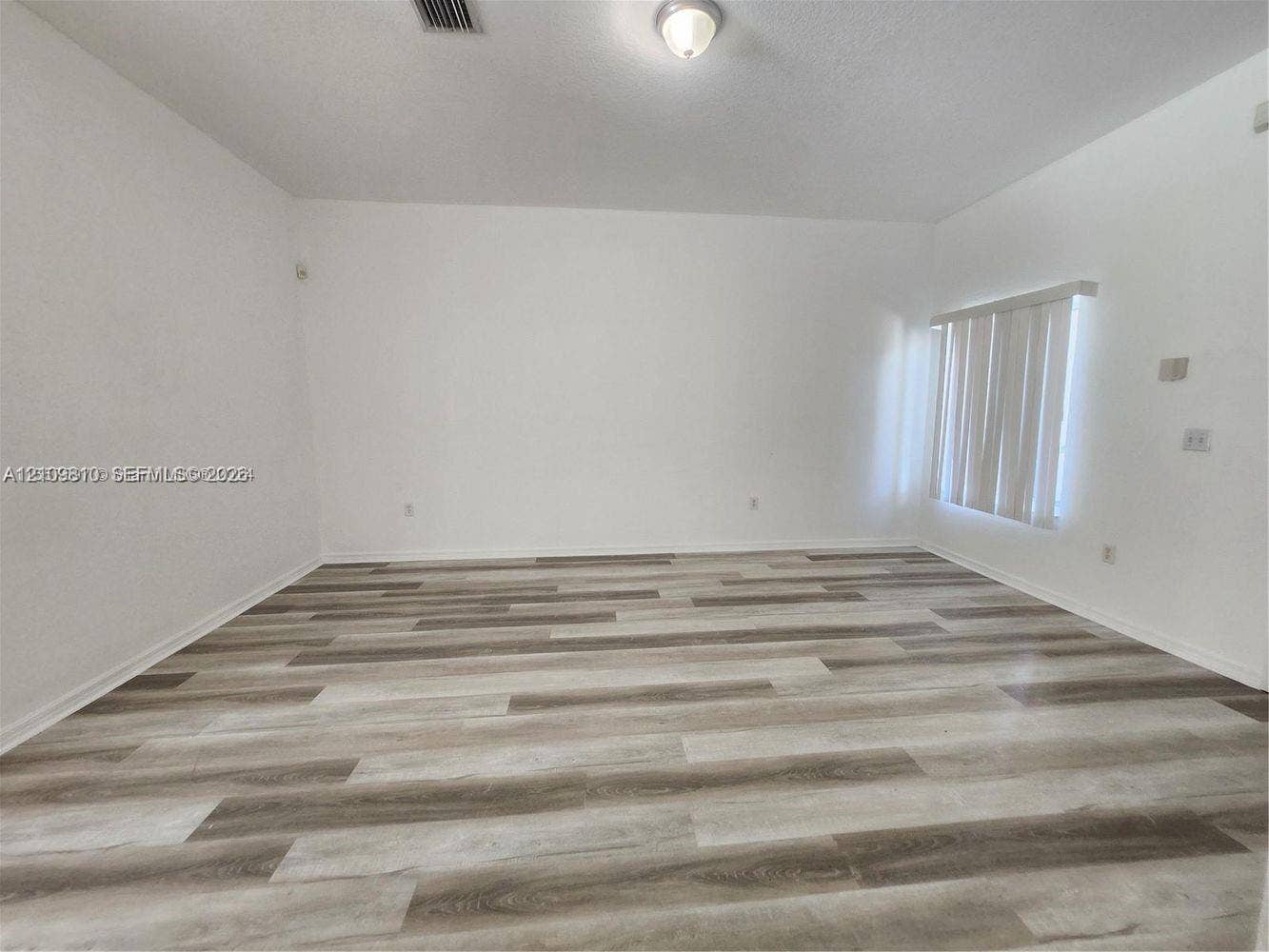 Interior space featuring wood-finish flooring, white walls, and vertical window blinds