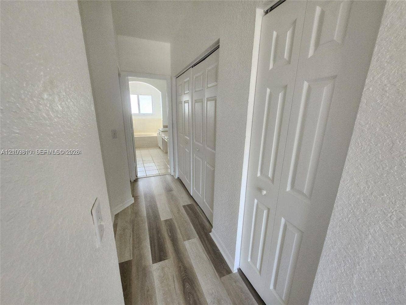 Hallway featuring wood-finish plank flooring and dual sets of bi-fold closet doors