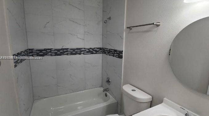 450 SW 2nd Street, #8, Pompano Beach, Pompano Beach, FL 33060 Bathroom featuring a tub-shower combination with large-format stone-pattern tile surround, horizontal mosaic tile accent strip, round wall-mounted mirror, and metal fixtures