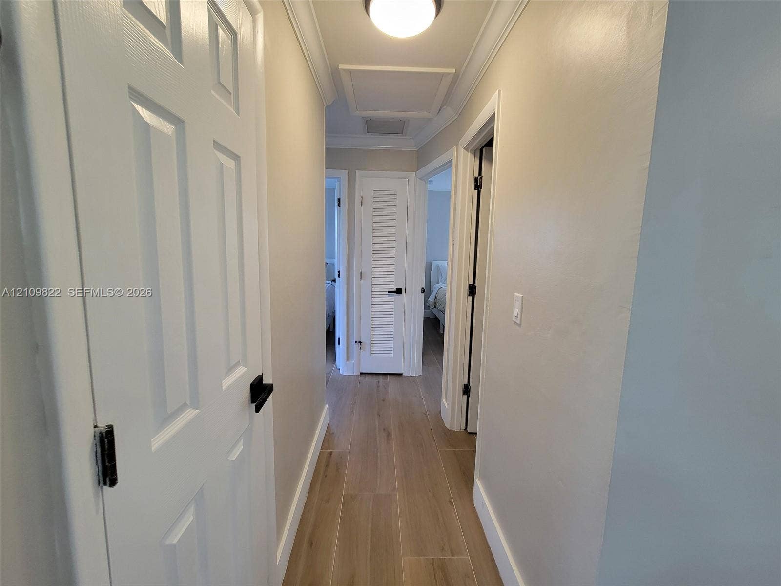 913 Lighthouse Drive, North Palm Beach, North Palm Beach, FL 33408 Hallway featuring wood-finish flooring, crown molding, multi-panel doors with matte black hardware, and a louvered closet door