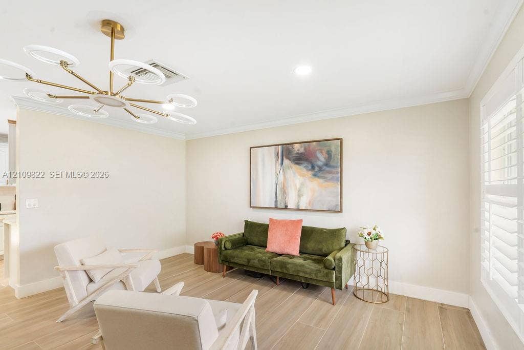 913 Lighthouse Drive, North Palm Beach, North Palm Beach, FL 33408 Spacious room featuring wood-finish tile flooring, crown molding, tiered gold-tone chandelier with integrated circular lighting, and plantation shutters