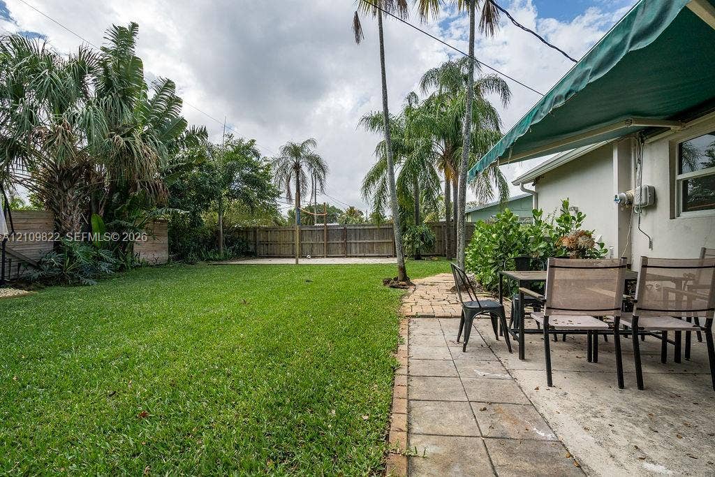 913 Lighthouse Drive, North Palm Beach, North Palm Beach, FL 33408 Rear patio featuring a retractable fabric awning, stone paver flooring, perimeter wood fencing, and mature palm trees
