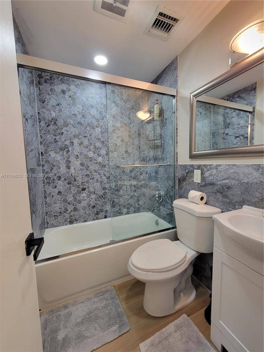913 Lighthouse Drive, North Palm Beach, North Palm Beach, FL 33408 Bathroom featuring a shower-tub combination with sliding glass doors, hexagon-patterned tile surround, vanity with an integrated basin, and framed wall mirror