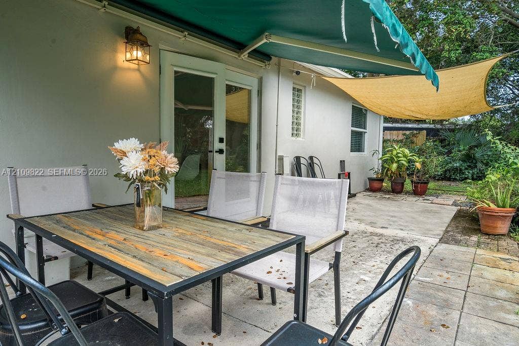 913 Lighthouse Drive, North Palm Beach, North Palm Beach, FL 33408 Concrete patio featuring a retractable green awning, overhead shade sail, wall-mounted lantern lighting, and glass-paneled double doors