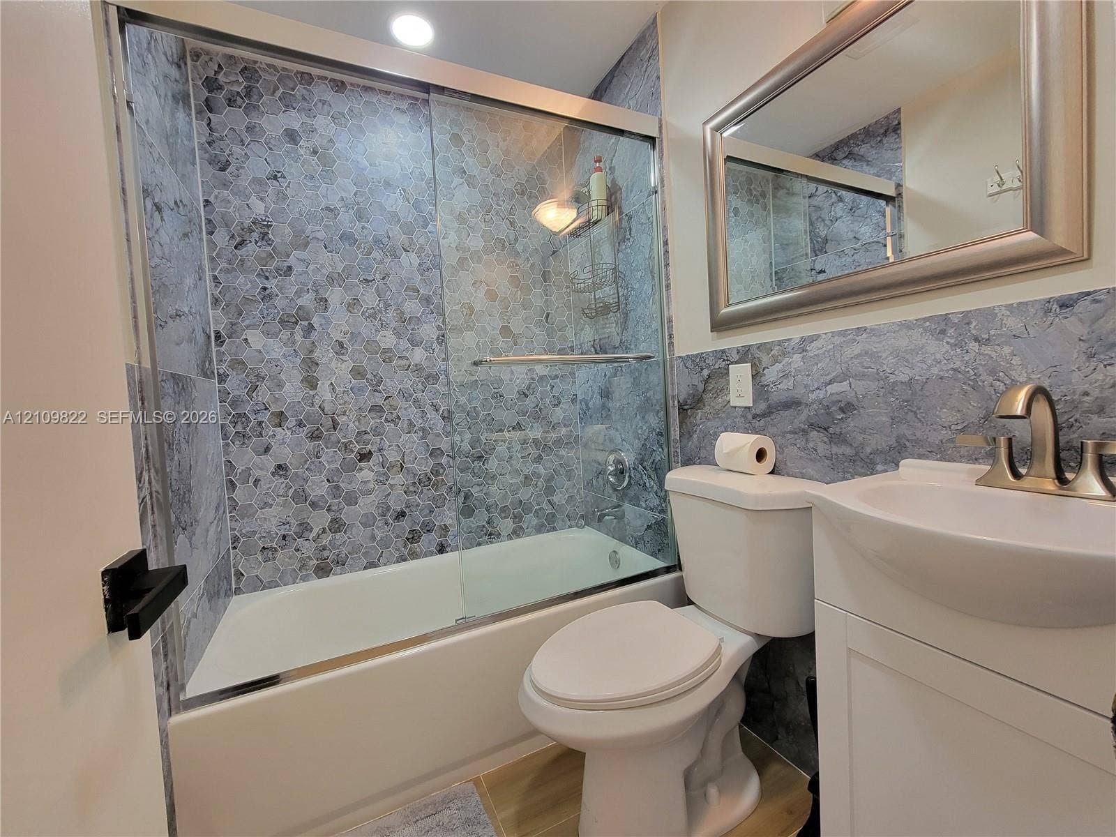 913 Lighthouse Drive, North Palm Beach, North Palm Beach, FL 33408 Full bathroom featuring a tub-shower combination with glass sliding doors, honeycomb-patterned tile surround, vanity with an integrated basin, brushed nickel faucet, and a wall-mounted mirror