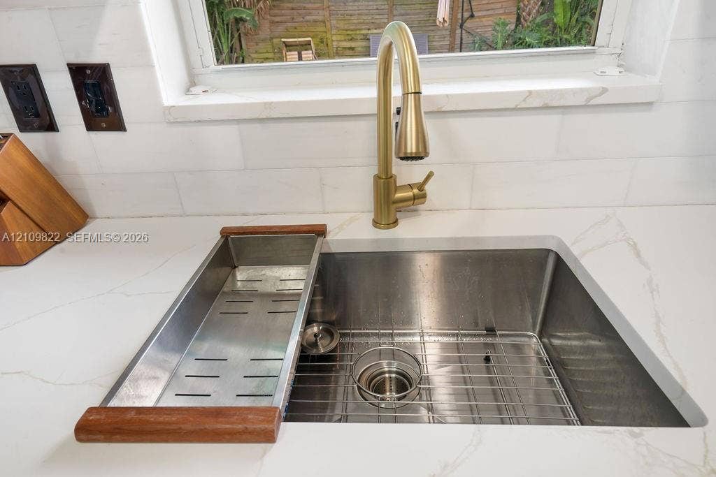 913 Lighthouse Drive, North Palm Beach, North Palm Beach, FL 33408 Undermount stainless steel kitchen sink featuring a brass high-arc pull-down faucet, stone-finish countertops, and subway-tile backsplash