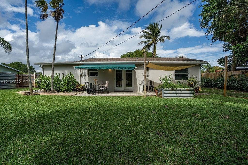 913 Lighthouse Drive, North Palm Beach, North Palm Beach, FL 33408 Expansive backyard featuring a manicured lawn, paved patio, retractable awning, mature palms, and metal raised garden beds
