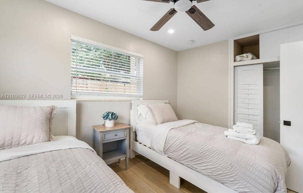 913 Lighthouse Drive, North Palm Beach, North Palm Beach, FL 33408 Neutral-toned room featuring wood-finish flooring, a ceiling fan with integrated lighting, a window with horizontal blinds, and a built-in closet with slatted doors and overhead shelving