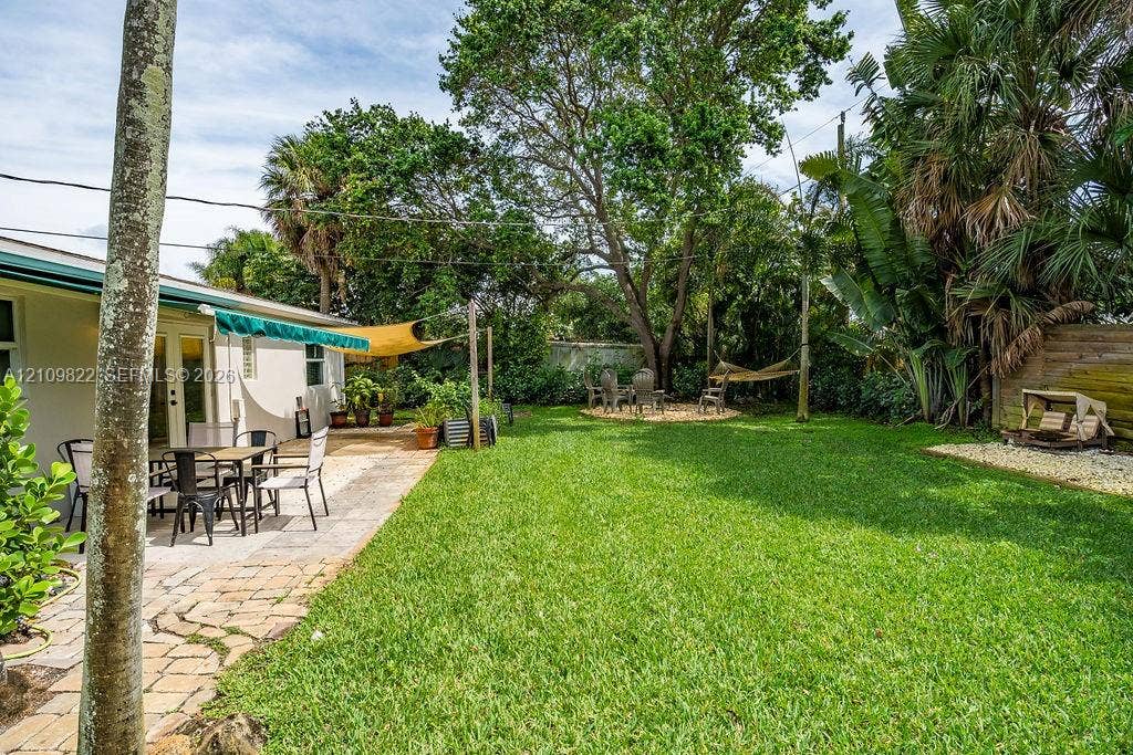 913 Lighthouse Drive, North Palm Beach, North Palm Beach, FL 33408 Backyard featuring a paved stone patio, mature canopy trees, lush lawn, and palm-lined perimeter