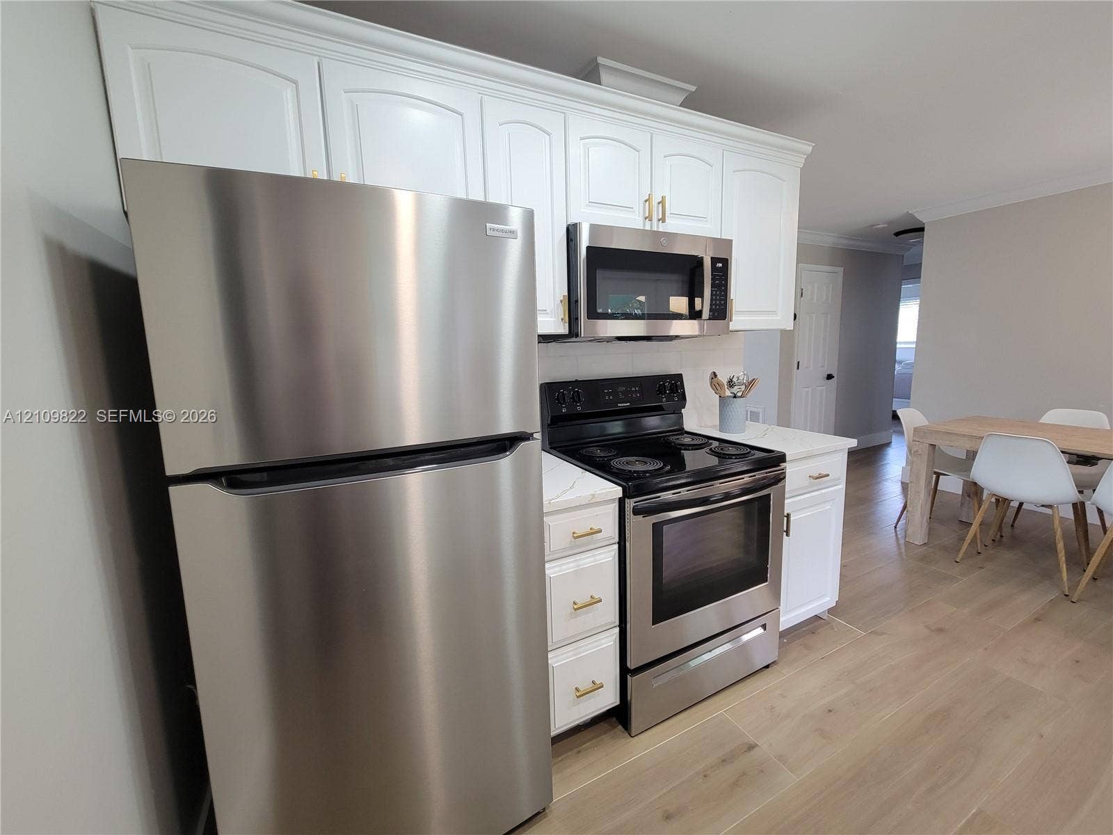 913 Lighthouse Drive, North Palm Beach, North Palm Beach, FL 33408 Kitchen featuring white shaker-style cabinetry with gold-toned hardware, stainless steel appliances, stone-finish countertops, and wood-finish flooring