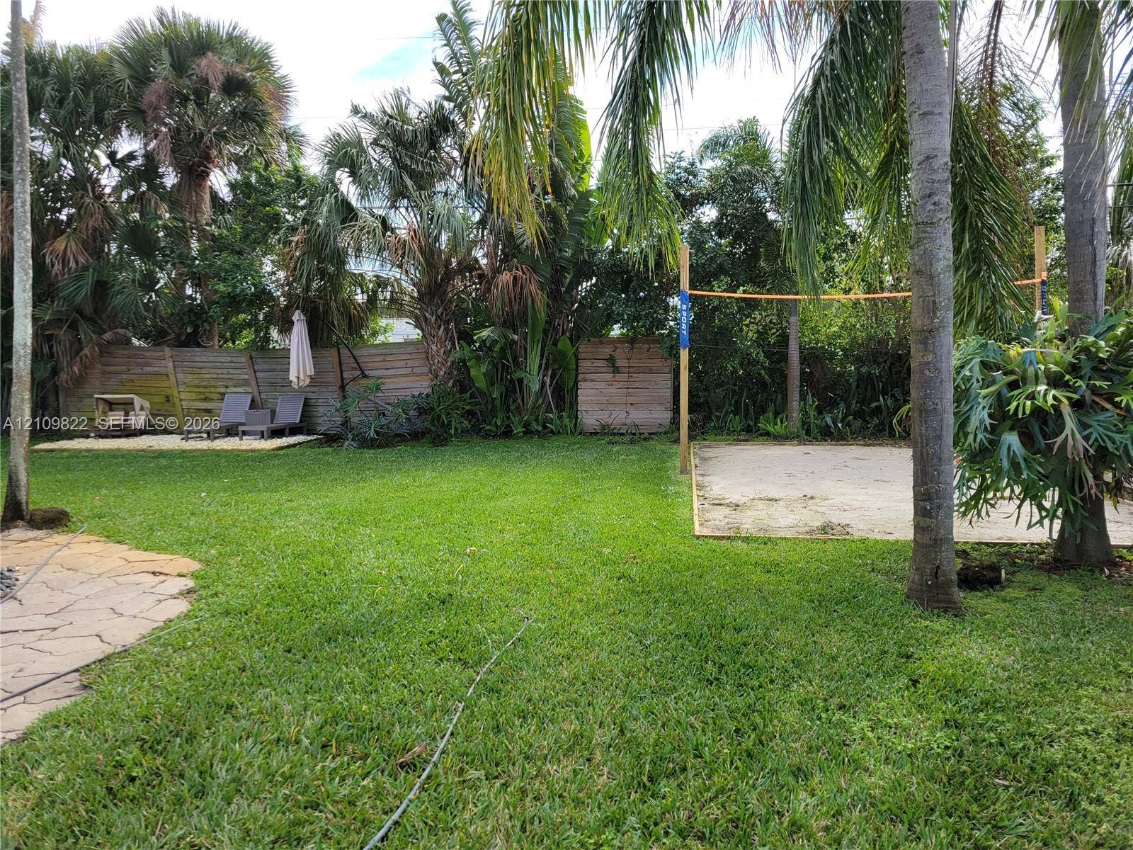 913 Lighthouse Drive, North Palm Beach, North Palm Beach, FL 33408 Expansive backyard featuring a natural stone patio, sand sports court, mature landscaping, and wood privacy fencing