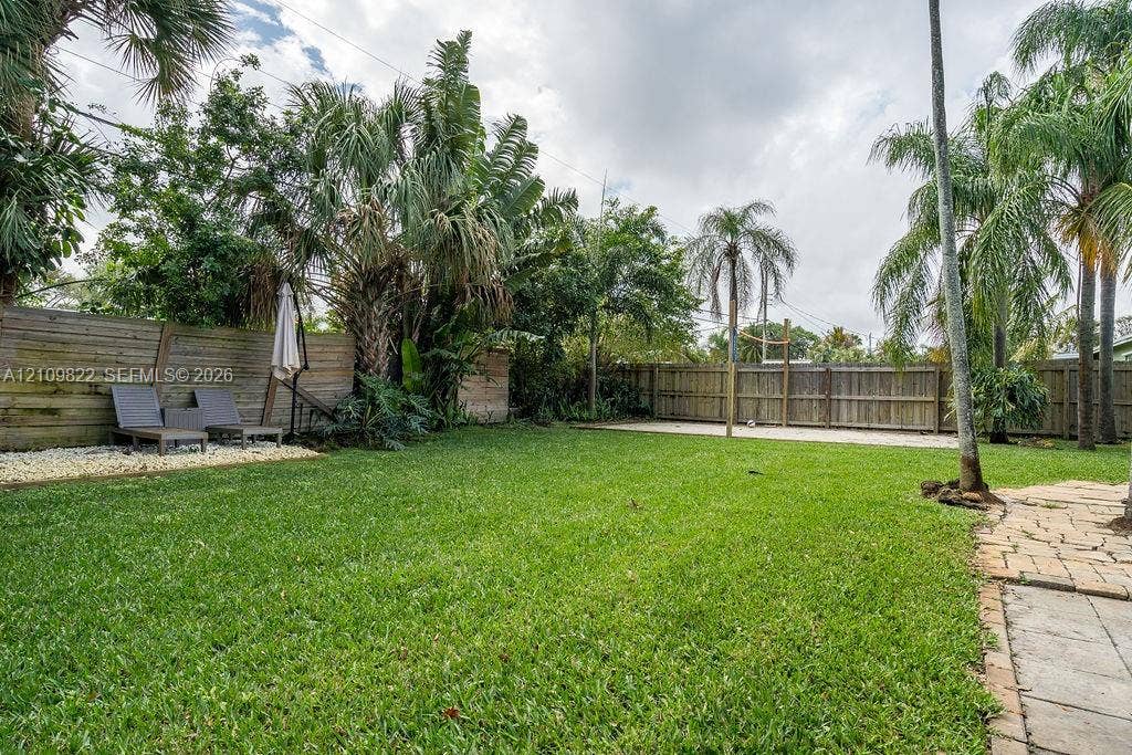 913 Lighthouse Drive, North Palm Beach, North Palm Beach, FL 33408 Expansive backyard featuring a lush lawn, mature palm trees, perimeter wood fencing, stone paver accents, and decorative pebble ground cover
