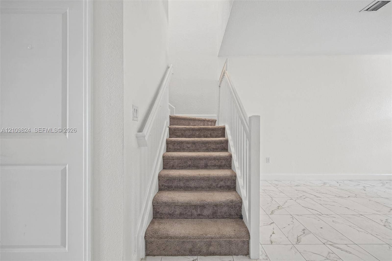 Staircase featuring carpeted steps, white balustrades, and a panel-style door, complemented by large-format tile flooring