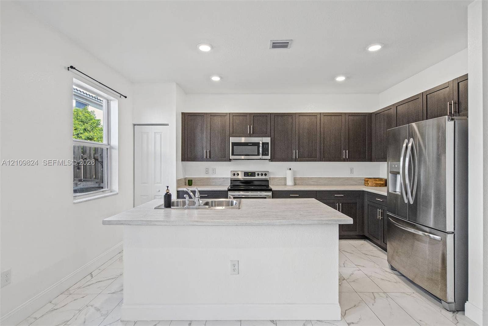 Kitchen featuring dark-toned cabinetry, a central island with a stone-finish countertop, stainless steel appliances, and tile flooring