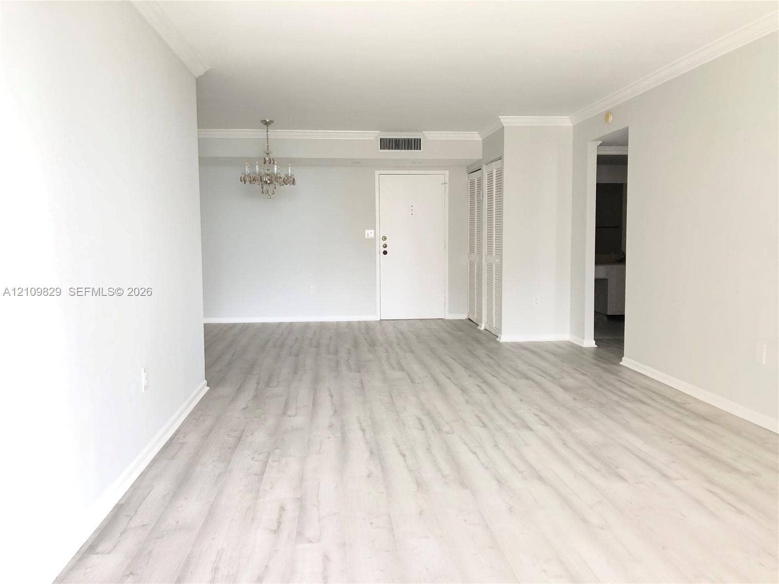 Open-concept interior featuring light wood-finish flooring, crown molding, and a suspended multi-arm light fixture