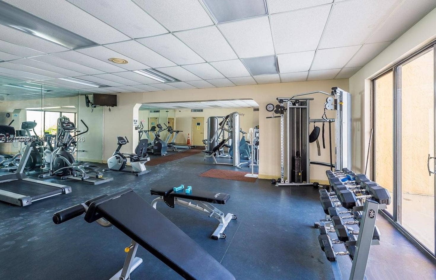 Fitness area featuring rubber flooring, drop ceiling with recessed lighting, floor-to-ceiling mirrors, and glass sliding doors