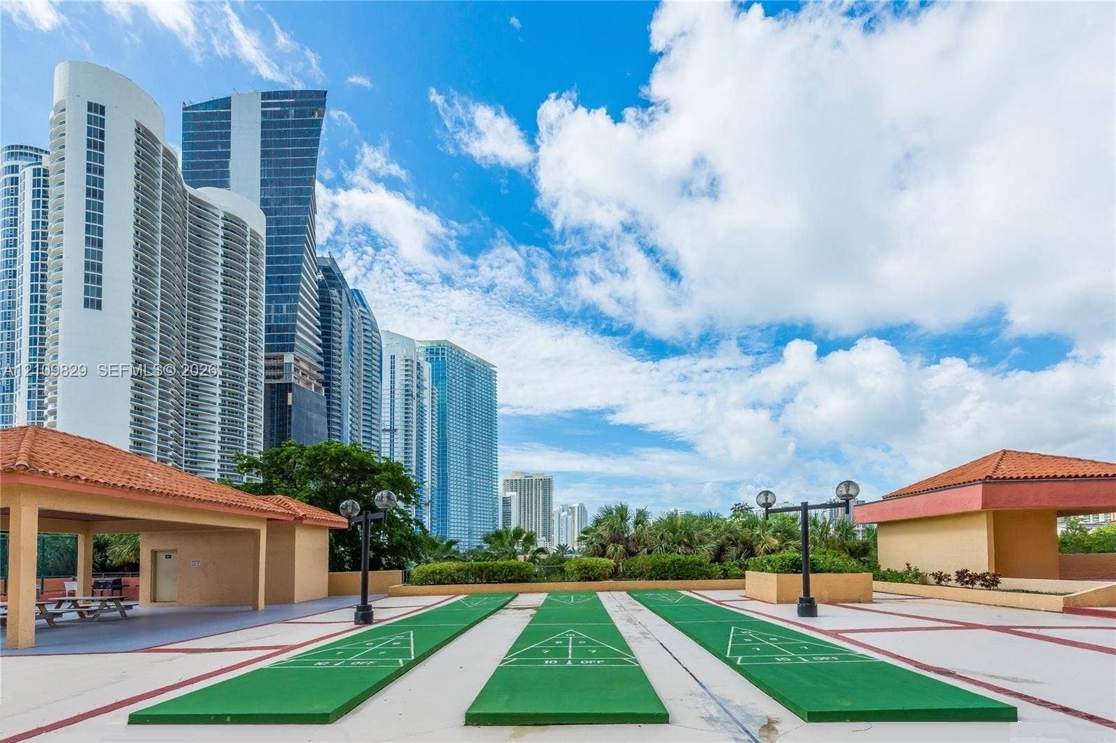 Recreational area featuring three painted shuffleboard courts, dual covered pavilions with terracotta-style roof tiles, and exterior lighting fixtures