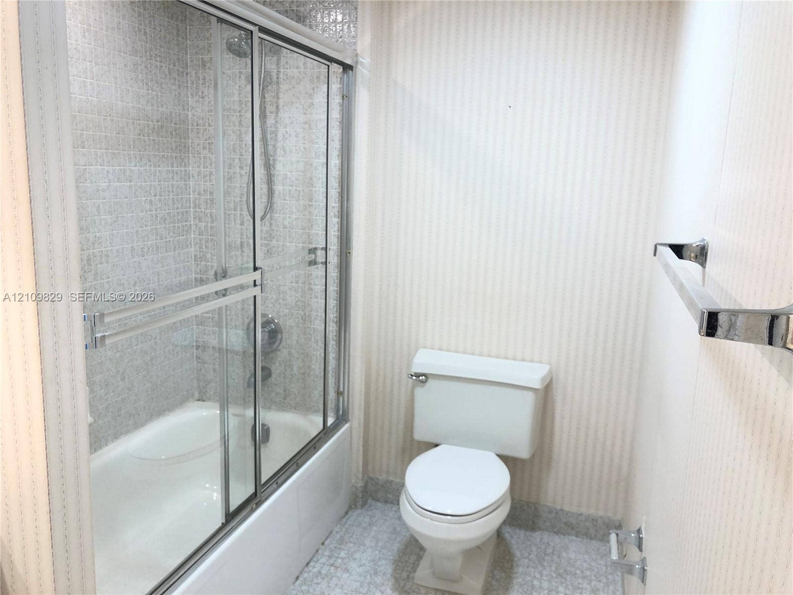 Shower-tub combination featuring a sliding glass enclosure, integrated chrome fixtures, mosaic-tiled shower surround, and a wall-mounted chrome towel bar