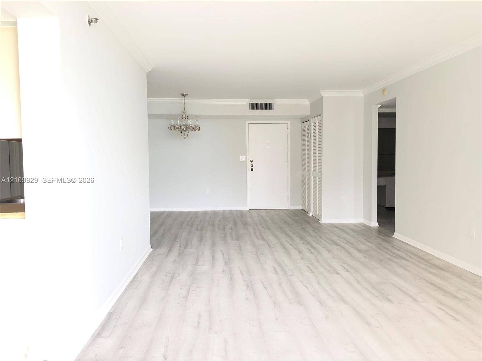 Open-concept interior featuring wood-finish flooring, crown molding, a decorative chandelier, and floor-to-ceiling louvered-door closets