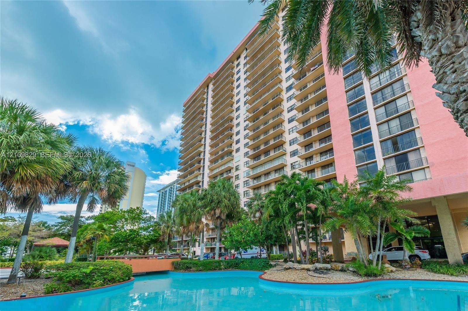 High-rise exterior featuring extensive balcony tiers, a turquoise swimming pool, and tropical landscaping