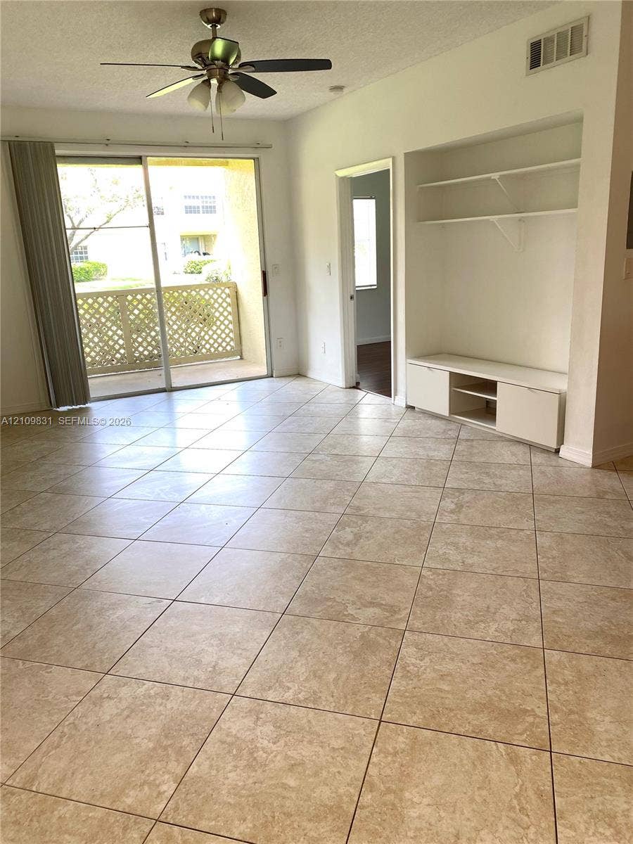Tiled flooring, built-in cabinetry with integrated shelving, sliding glass door, ceiling fan with light fixture, and covered balcony with lattice railing