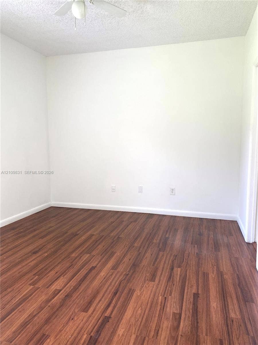 Room featuring wood-finish flooring, white walls, and a ceiling fan