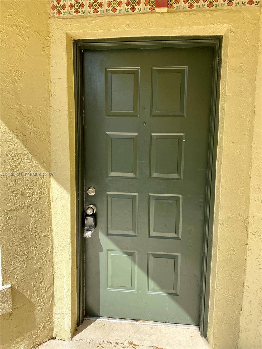 Eight-panel entry door featuring a matte green finish, textured stucco exterior walls, and decorative patterned tile trim