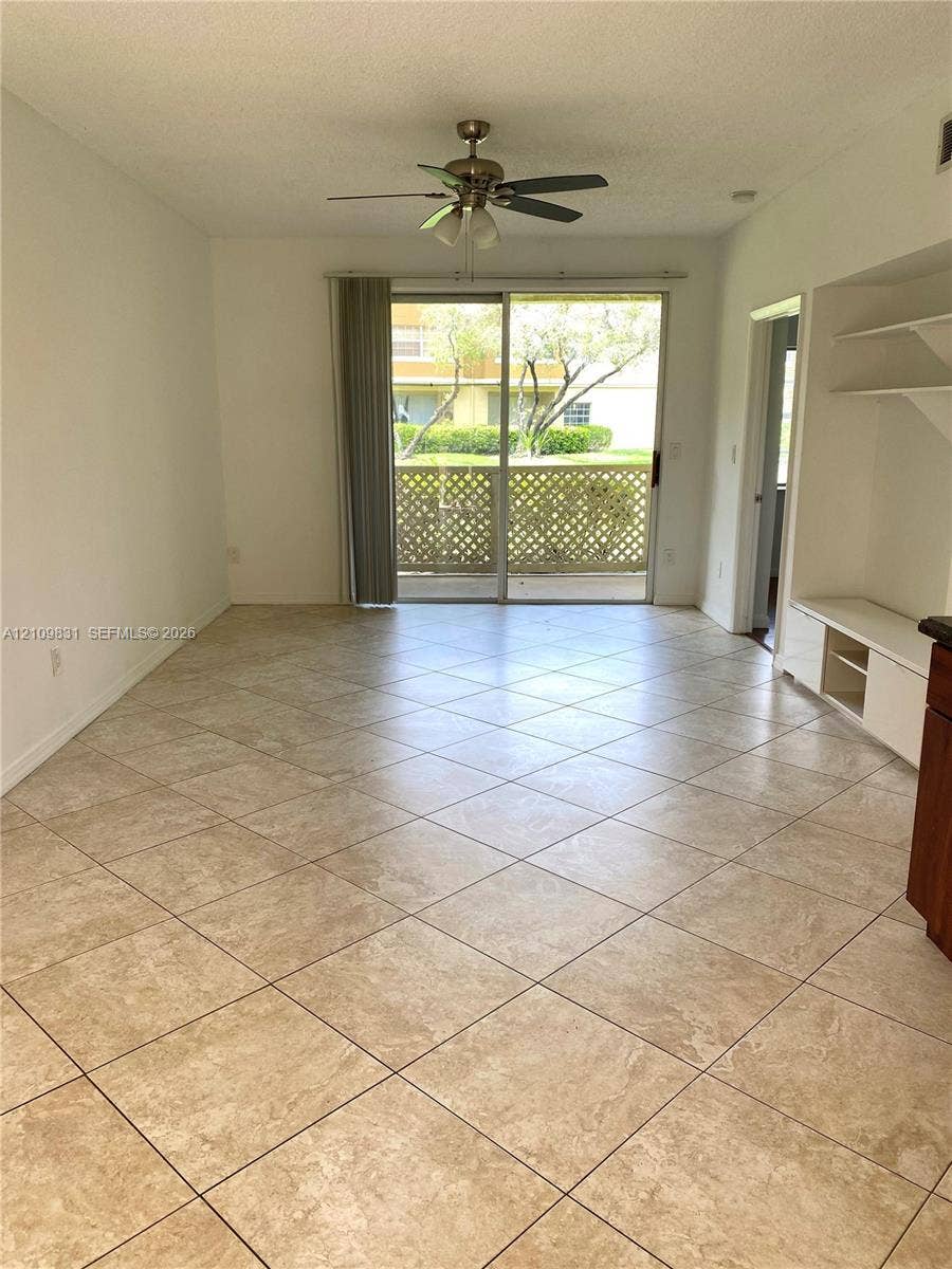 Tiled flooring laid in a diagonal pattern, sliding glass doors, built-in shelving, and a ceiling fan