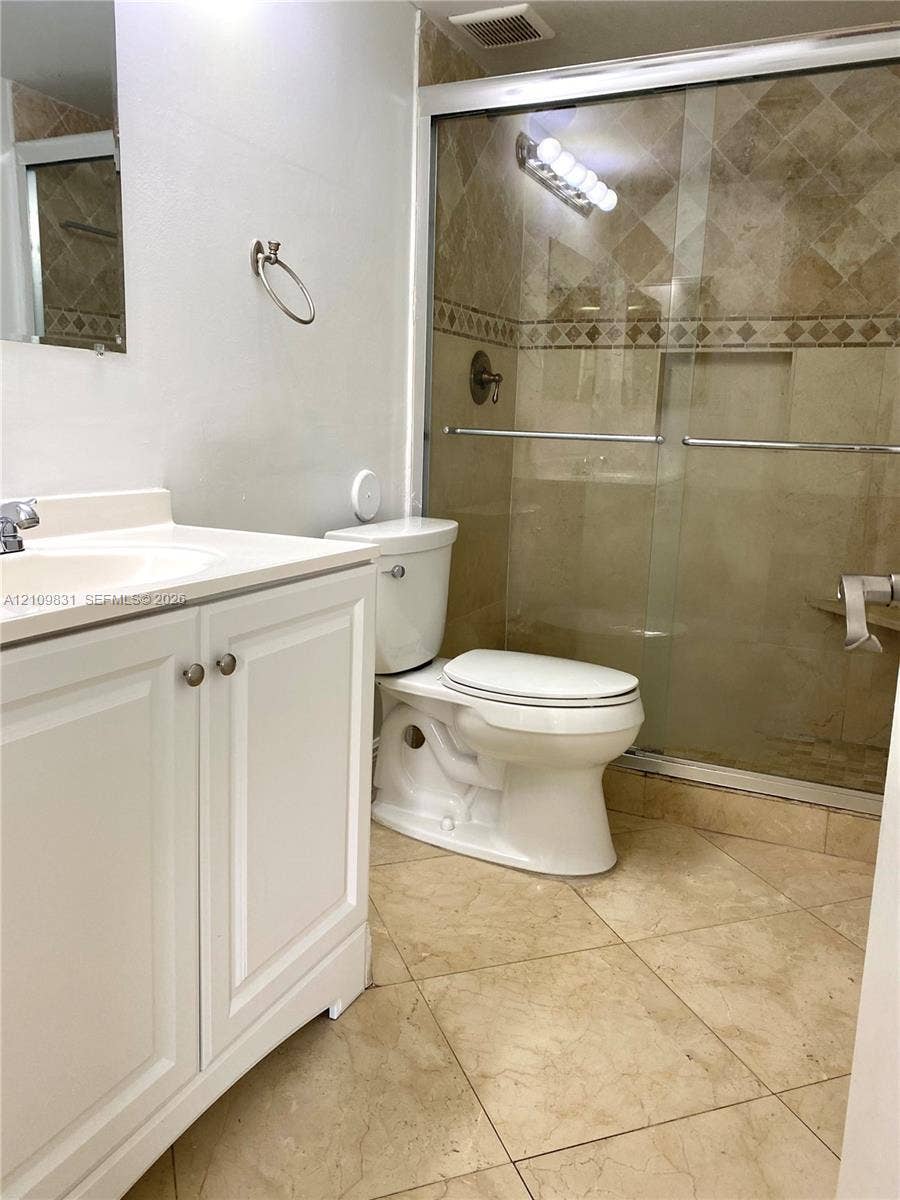 Bathroom featuring a white vanity cabinet, solid-surface countertop, tiled shower enclosure with sliding glass doors, and diagonal-pattern floor tiling