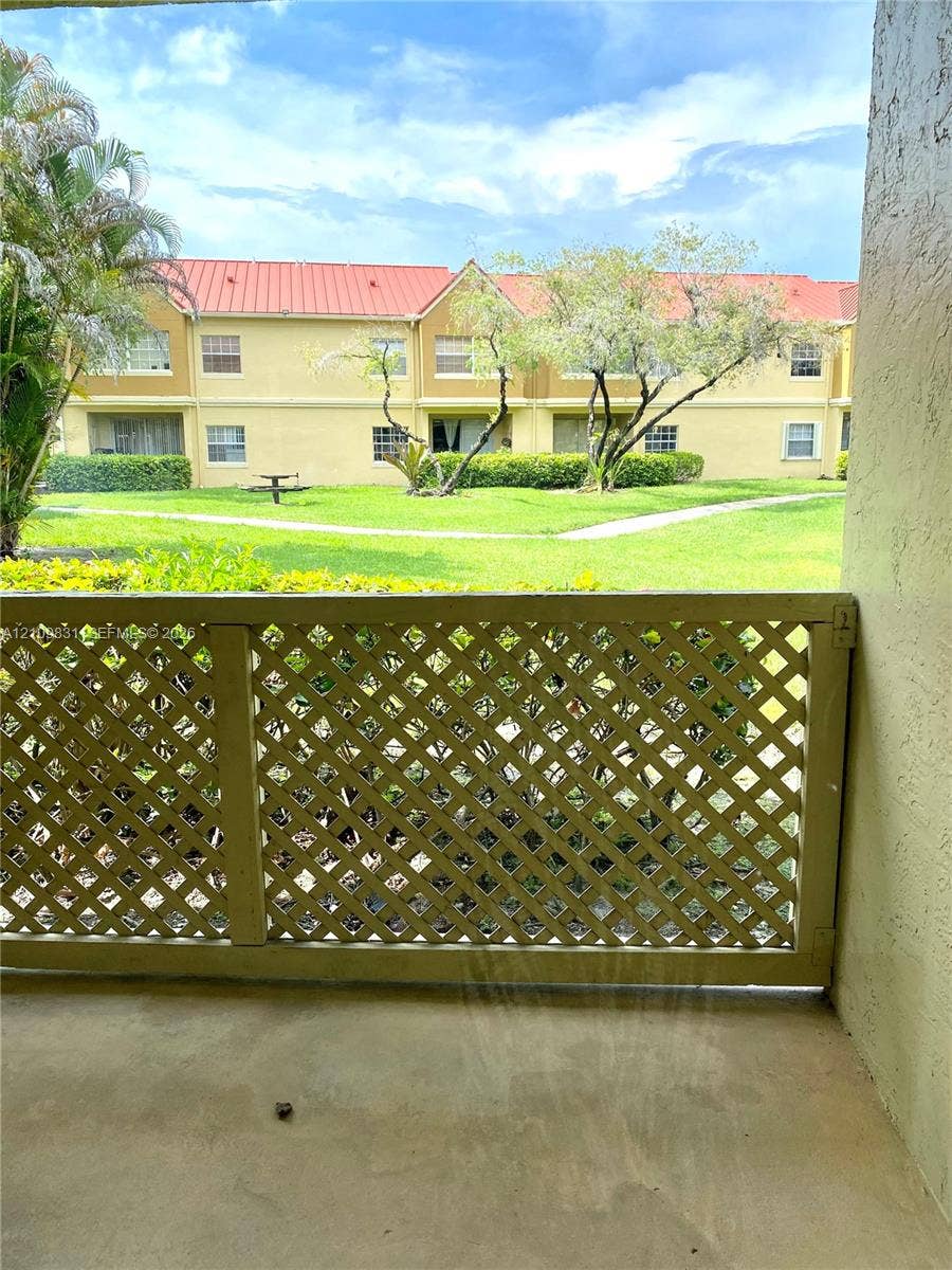 Covered balcony featuring a decorative wood lattice railing, concrete flooring, and greenery