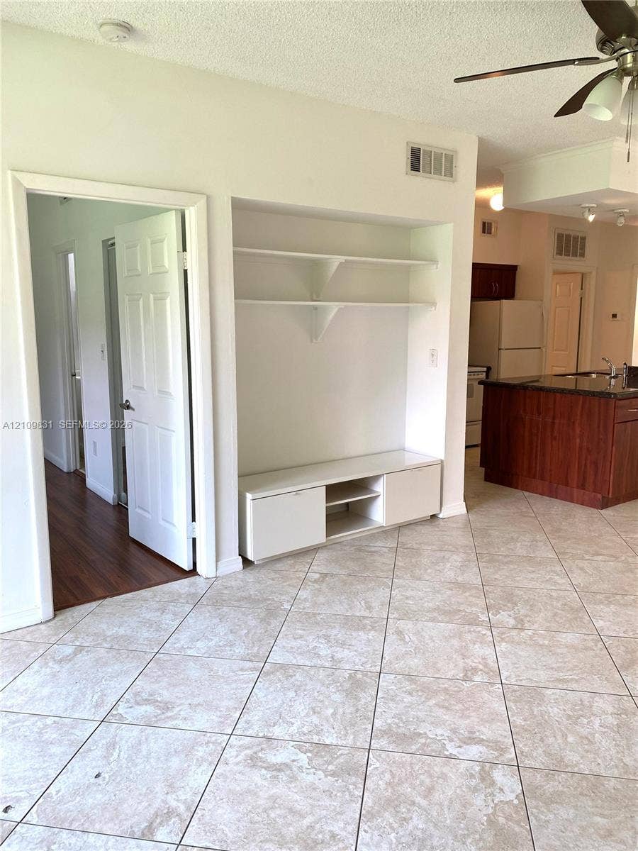 Built-in recessed shelving unit with lower cabinetry, neutral-toned tile flooring, and a ceiling-mounted fan