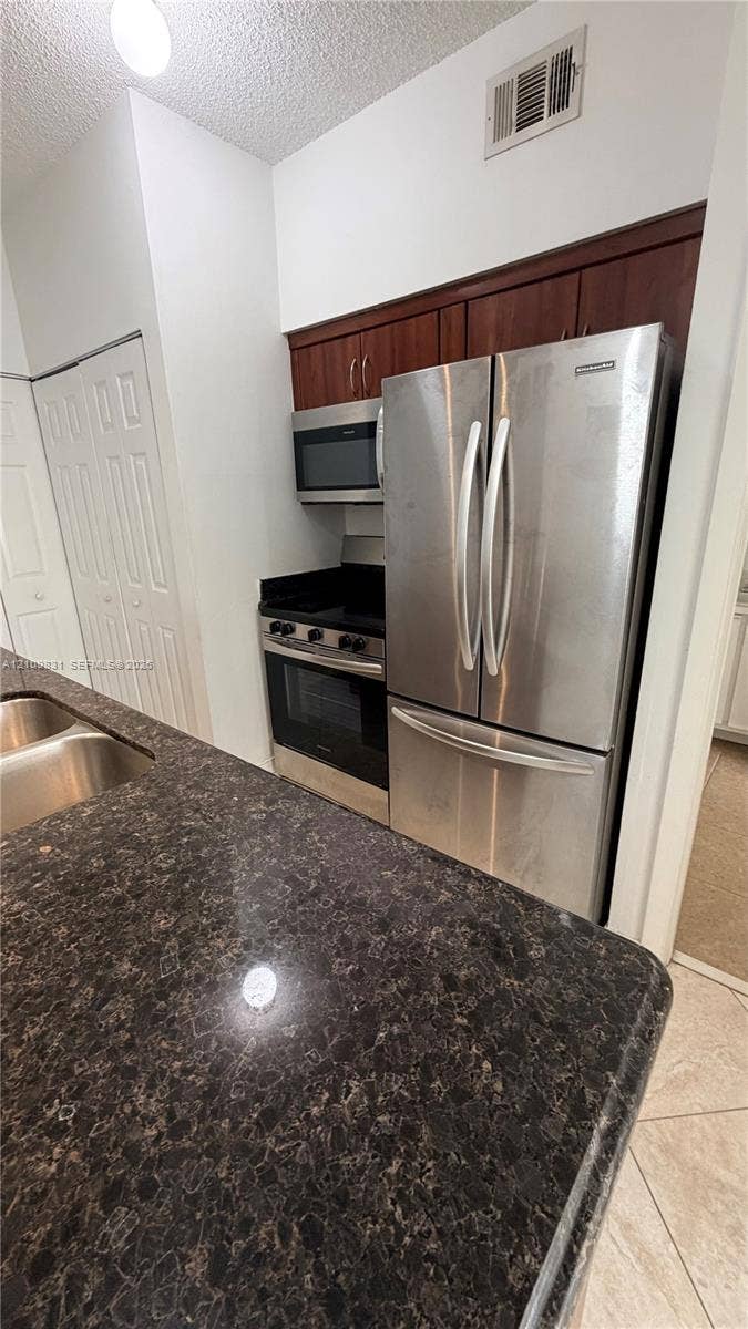 Kitchen area featuring dark stone countertops, stainless steel appliances, dark wood-finish cabinetry, and a double-basin stainless steel sink