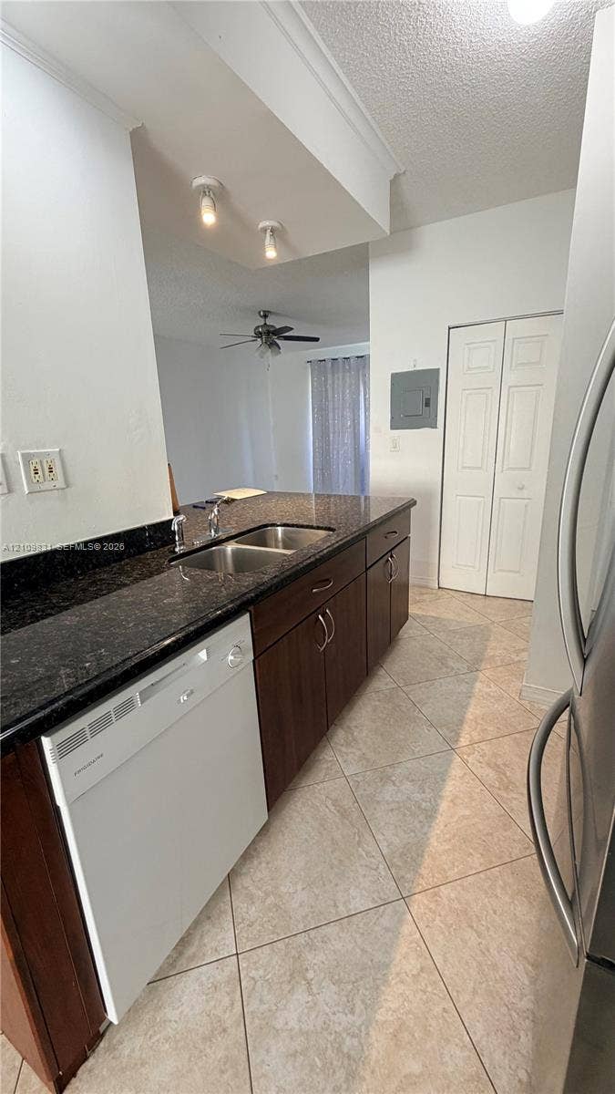 Kitchen featuring dark-toned cabinetry, stone-finish countertops, stainless steel dual-basin sink, tile flooring laid on a diagonal, and built-in dishwasher