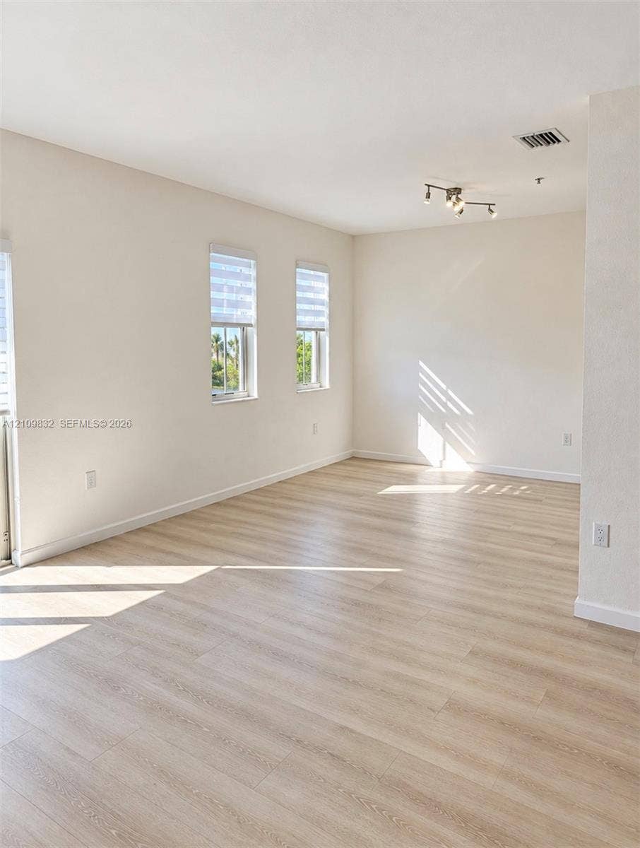 8800 NW 97th Avenue, #205, Doral, FL 33178 Neutral interior space featuring wood-finish flooring, crisp white walls, dual windows with roller shades, and a multi-directional track lighting fixture