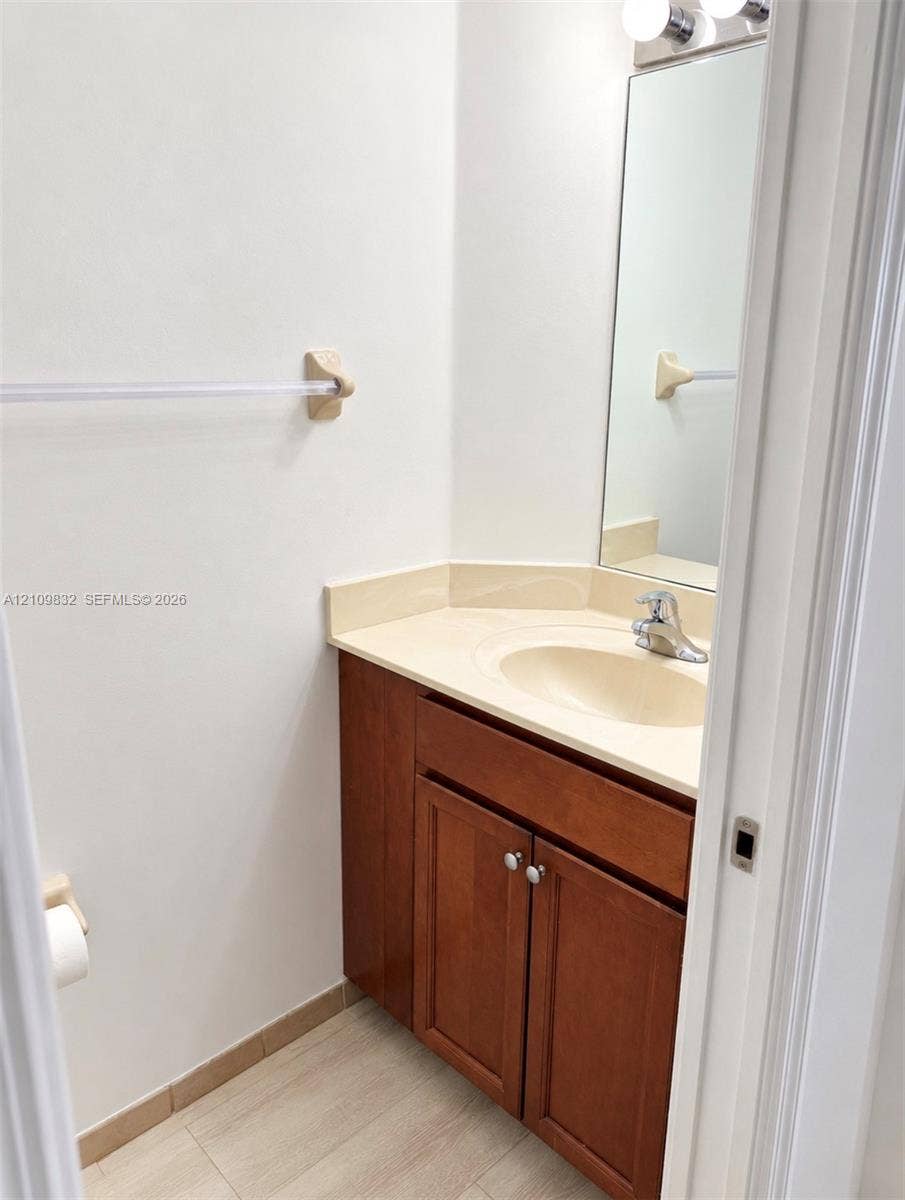 8800 NW 97th Avenue, #205, Doral, FL 33178 Wood-finish cabinetry, solid-surface countertop with integrated oval basin, polished chrome faucet, rectangular wall-mounted mirror, and multi-light fixture